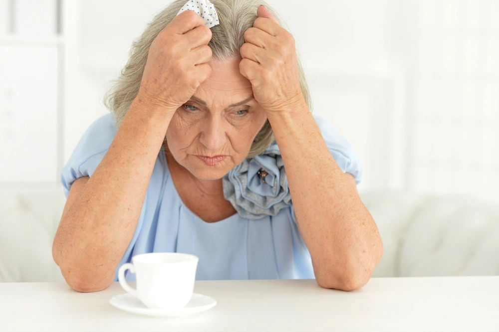 Ältere Dame blickt gedankenverloren ins Leere mit einer leeren Tasse vor ihr